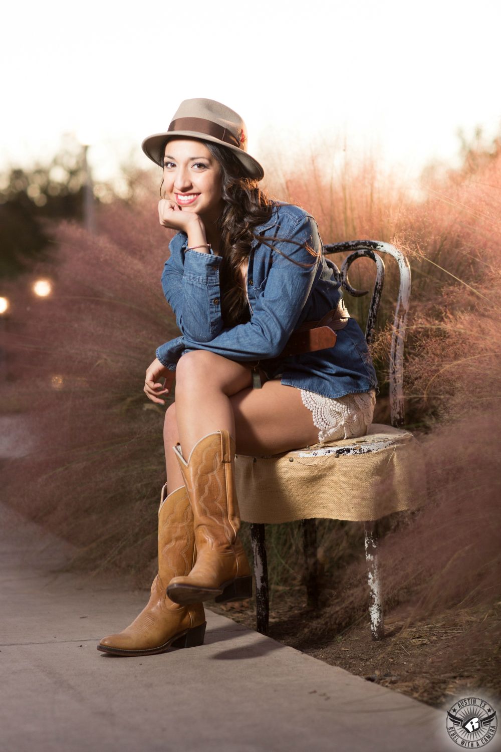The best senior portraits in Austin of trendy girl in denim shirt and cowboy boots with cute hat at Butler Park.