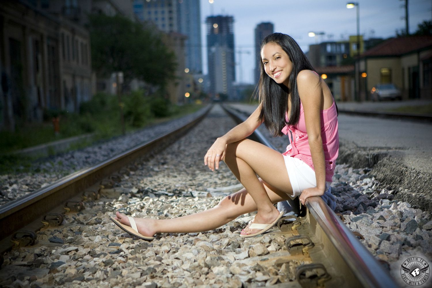 Best senior portrait photographers Austin take a picture of girl in white shorts and pink tank top on the railroad tracks in downtown Austin.