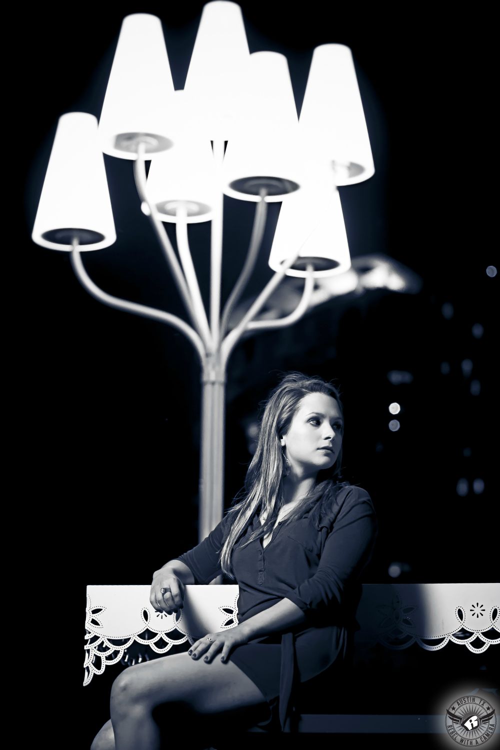 Senior photographers in Austin take black and white picture of girl in blue dres at night under unique lampstand near the Lamar Pedestrian Bridge.