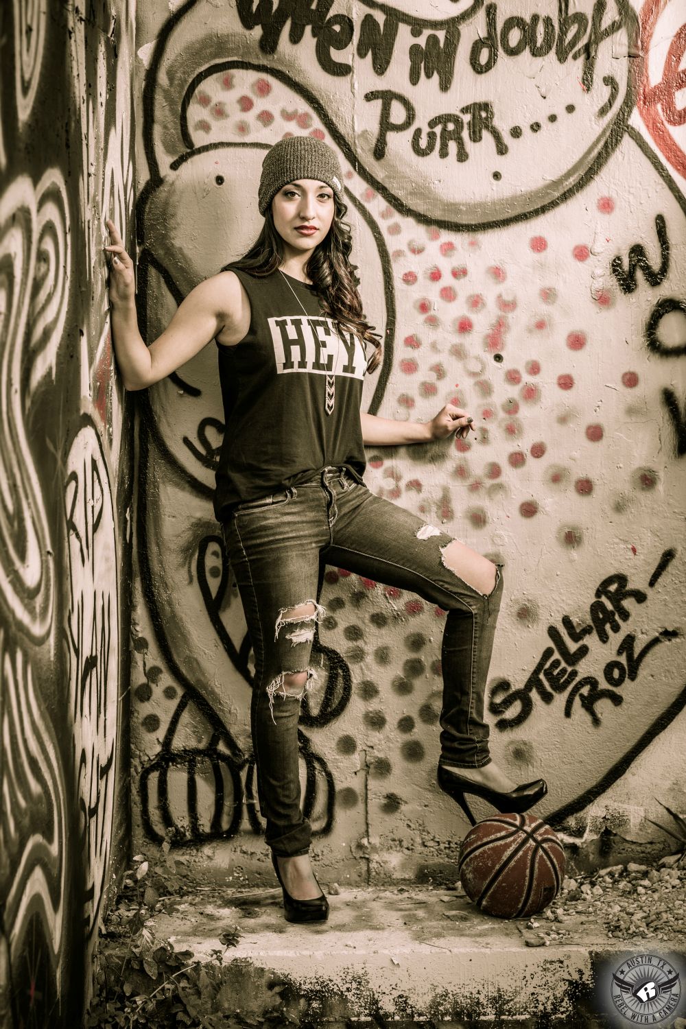 Urban high school senior portrait photography of girl in ripped jeans and high heels with hair and makeup by Divaz Fabula at the Castle Hill Graffiti Wall in Austin, Texas.