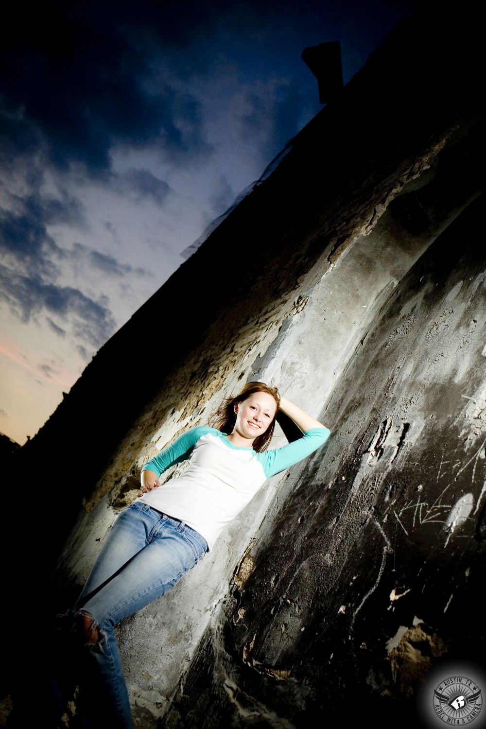 Amazing high school senior portraits in Austin downtown in the Warehouse District of girl in jeans against old wall with dramatic sunset.