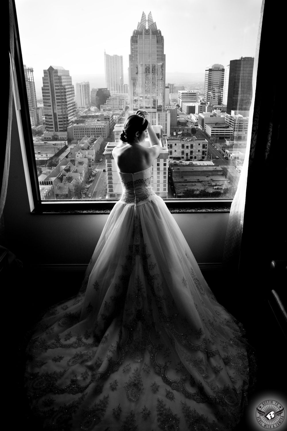 Bride in classic strapless gown with gold accents looks out over the Austin skyline from the Hilton Hotel in downtown Austin before her wedding at the Austin Club.