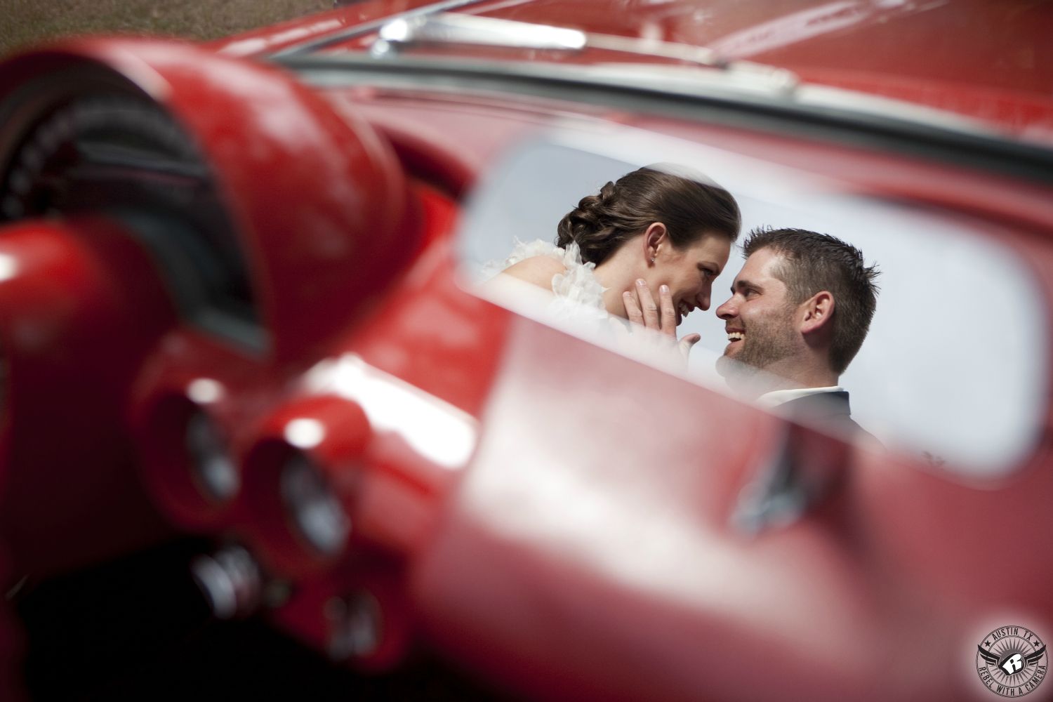 Groom looks lovingly at bride in rear view mirror of sporty red vintage Corvette convertable at Kindred Oaks Austin wedding venue after their wedding ceremony.