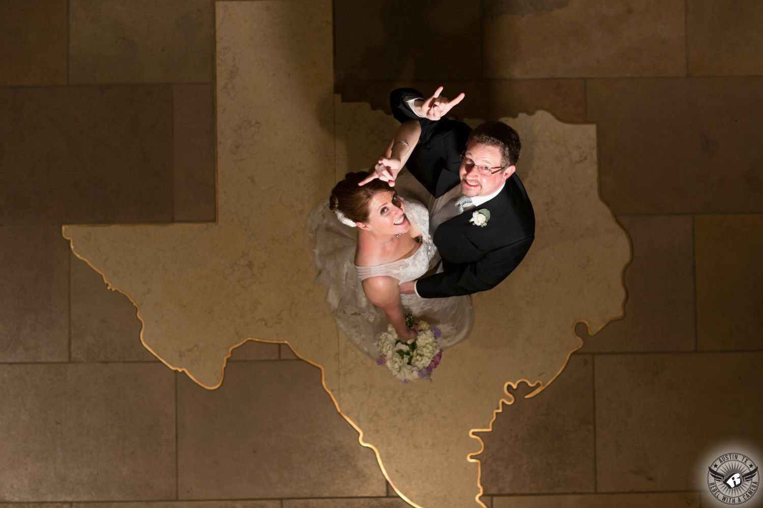 Longhorn bride in strapless dress and groom in black tuxedo hook 'em horns in Texas state outline at AT&T Executive Education and Conference Center on the University of Texas campus during their wedding reception in Austin texas coordinated by Barbara's Brides.