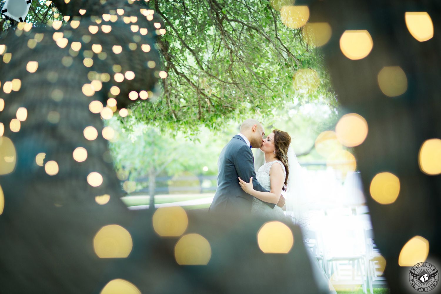 Bride in sparkly wedding dress and groom kiss passionately at their Austin wedding surrounded by the bokeh of twinkly lights in the trees at Antebellum Oaks Austin area wedding venue in Lakeway.