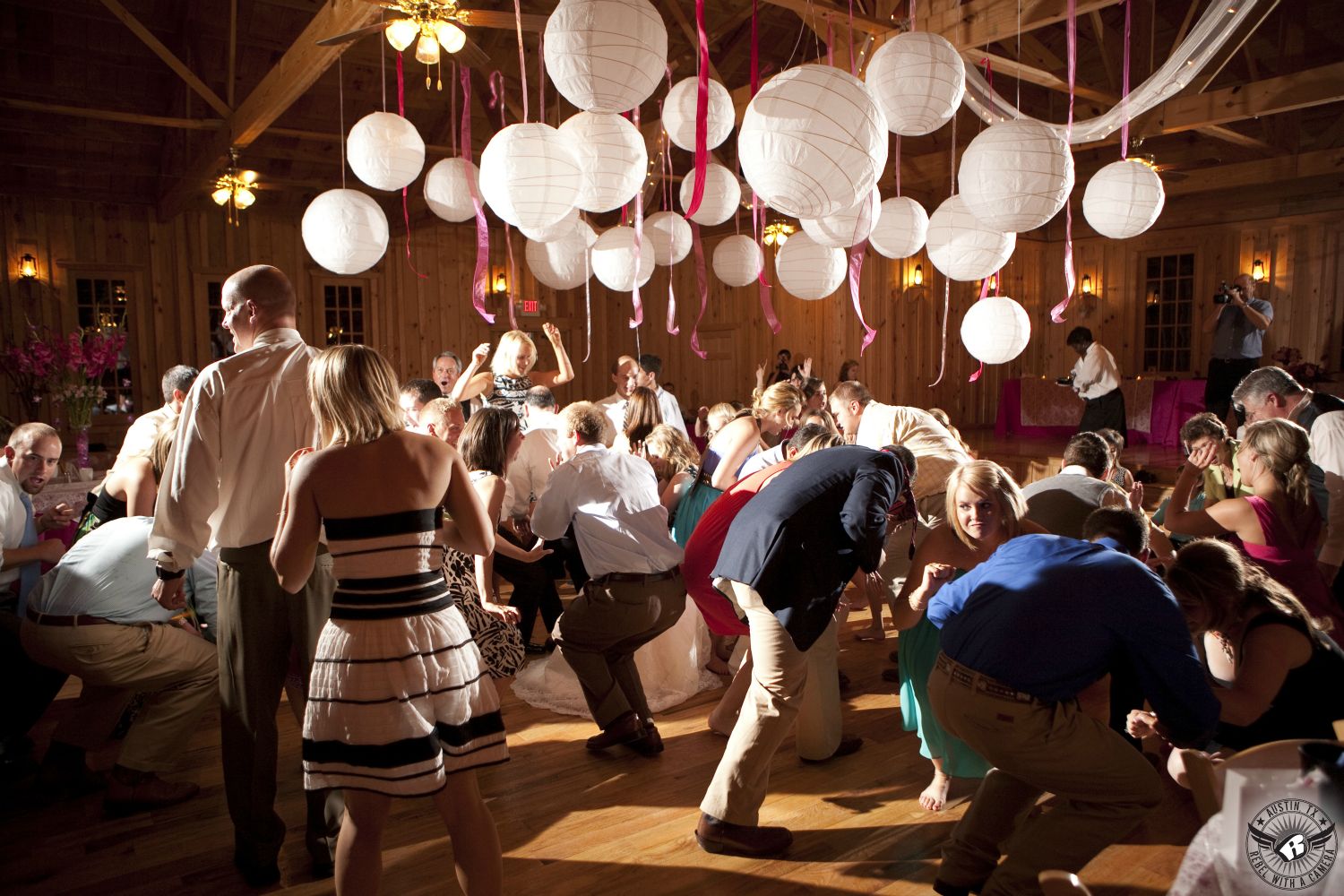 Festive guests dancing under white paper lanterns and pink ribbons at wedding reception at the rustic Texas Old Town Austin area wedding venue.