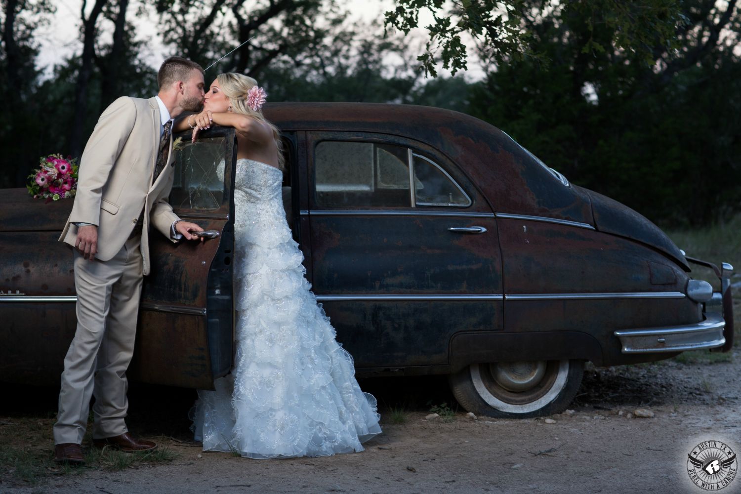 Picture of bride in gorgeous strapless lace wedding dress and groom kissing in front of vintage car at Vista West Ranch Dripping Springs wedding venue taken by Austin wedding photographer.