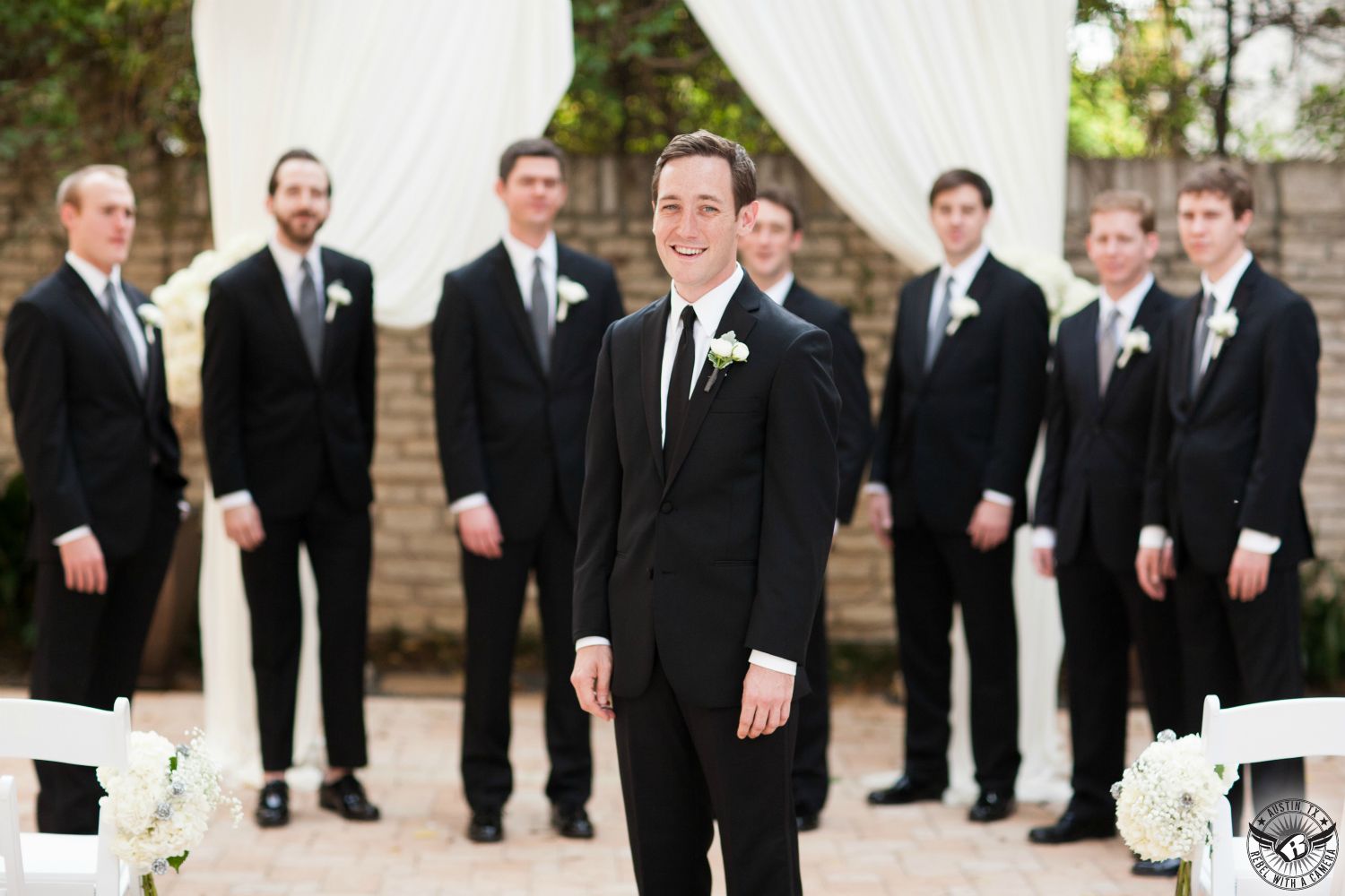 wedding photo of groom and groomsmen in black tuxedos at wedding ceremony site at Texas Federation of Women's Clubs Headquarters Mansion Austin wedding venue taken by austin wedding photographer.