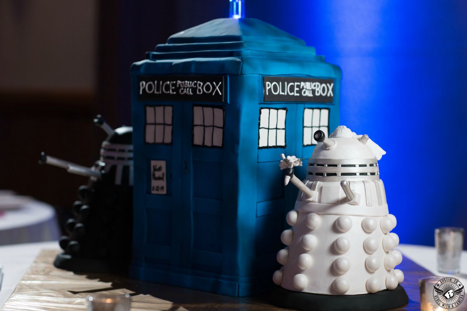 Picture of Dr Who TARDIS wedding cake with bride and groom Daleks by  The Cake Plate Austin with royal blue uplighting coordinated by Barbara's Brides at the AT&T Executive Education and Conference Center taken by Austin wedding photographer.
