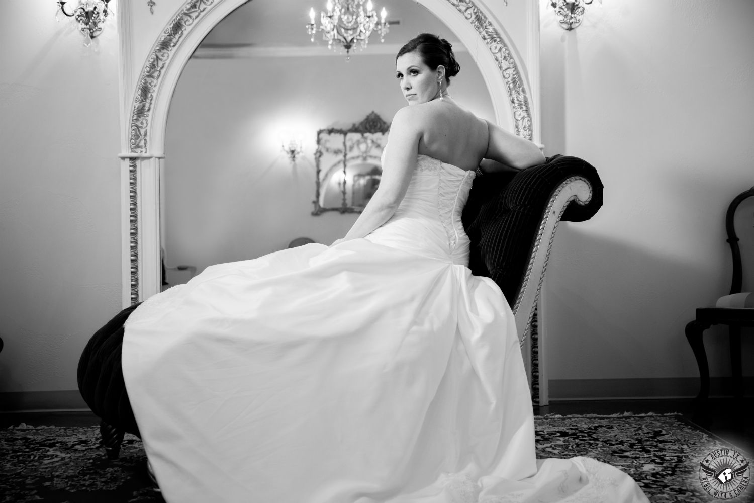 Black and white image of back of dramatic bride sitting on elegant divan in front of large mirror in the bridal room at Villa St. Clair Austin wedding venue. 