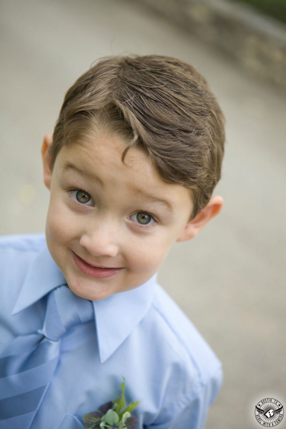 Happy picture of adorable ring bearer in light blue shirt and tie with delicate boutonniere by Visual Lyrics Floral Artistry smiles at the camera just before the wedding ceremony at Nature's Point Austin area wedding venue on the shores of Lake Travis.