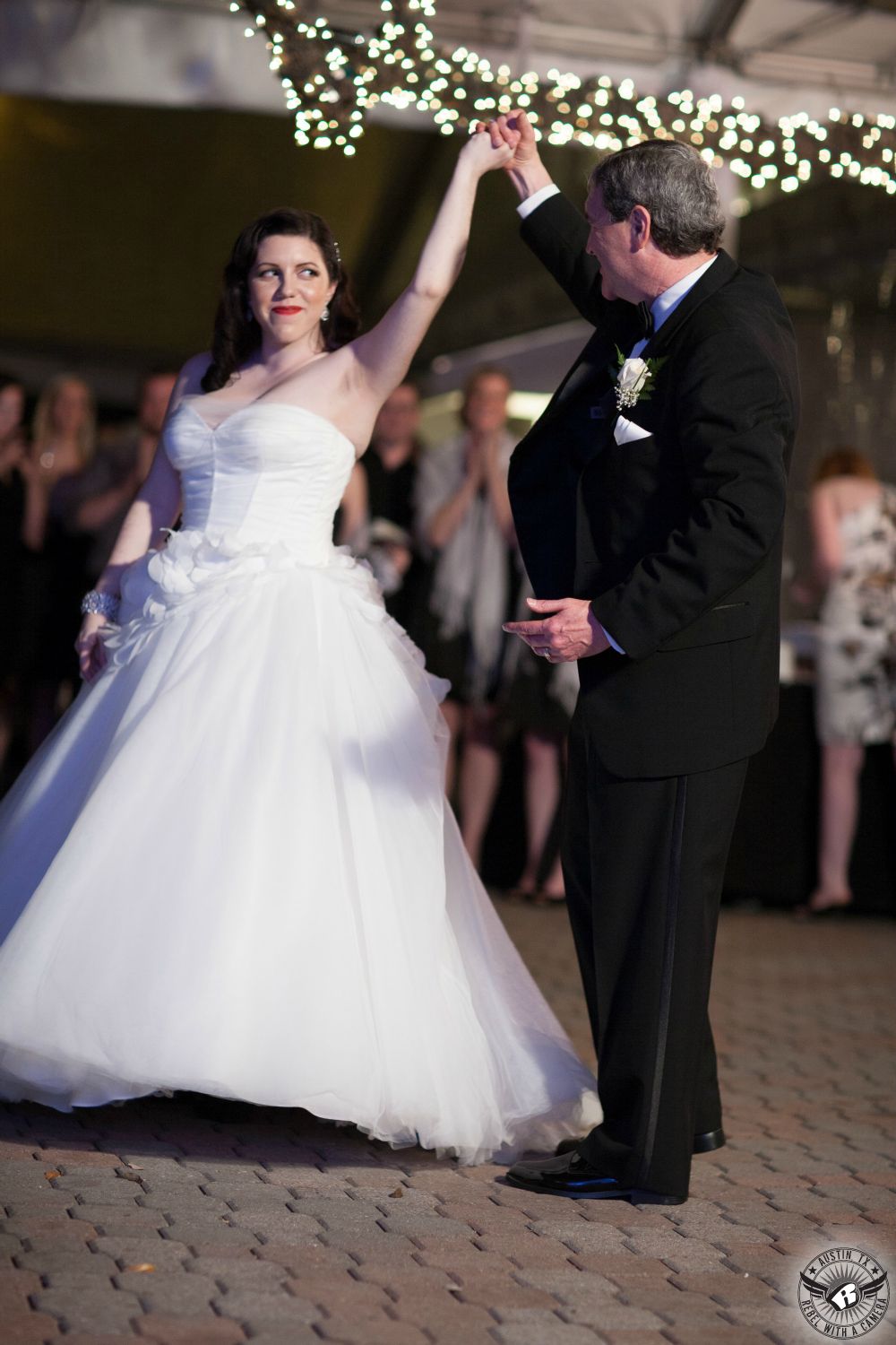 Picture of happy bride in White by Vera Wang wedding gown from David's Bridal and red lipstick and her father in black tuxedo dancing the father-daughter dance at the wedding reception under the winter tent with twinkly lights in the trees at the Allan House wedding venue in downtown Austin, Texas.