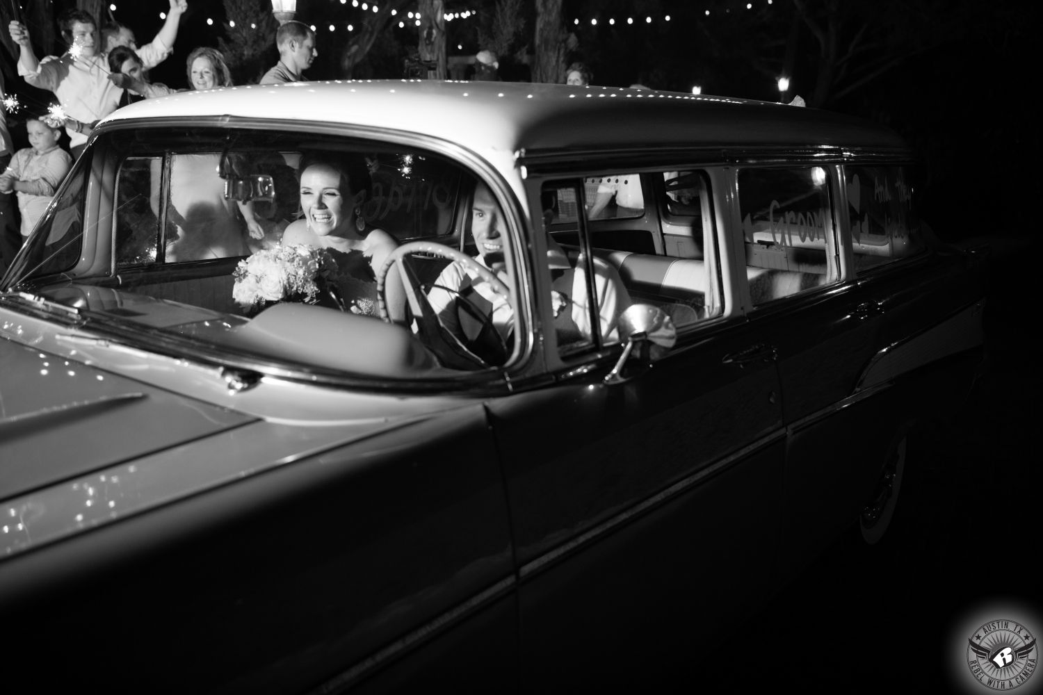 Black and white image of bride and groom exiting their wedding reception at Nature's Point austin wedding venue in restored vintage station wagon taken by Austin wedding photographer.