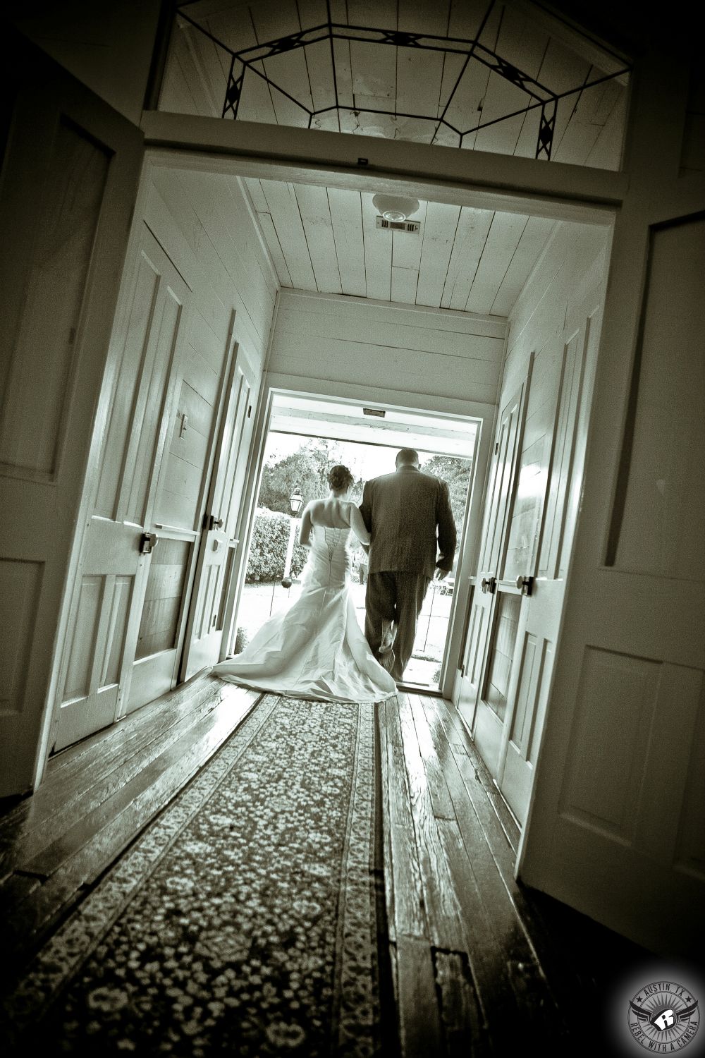 Black and white image of back of bride and her father walking through door of the bride's room on their way to the wedding ceremony at Inn at Salado wedding venue.