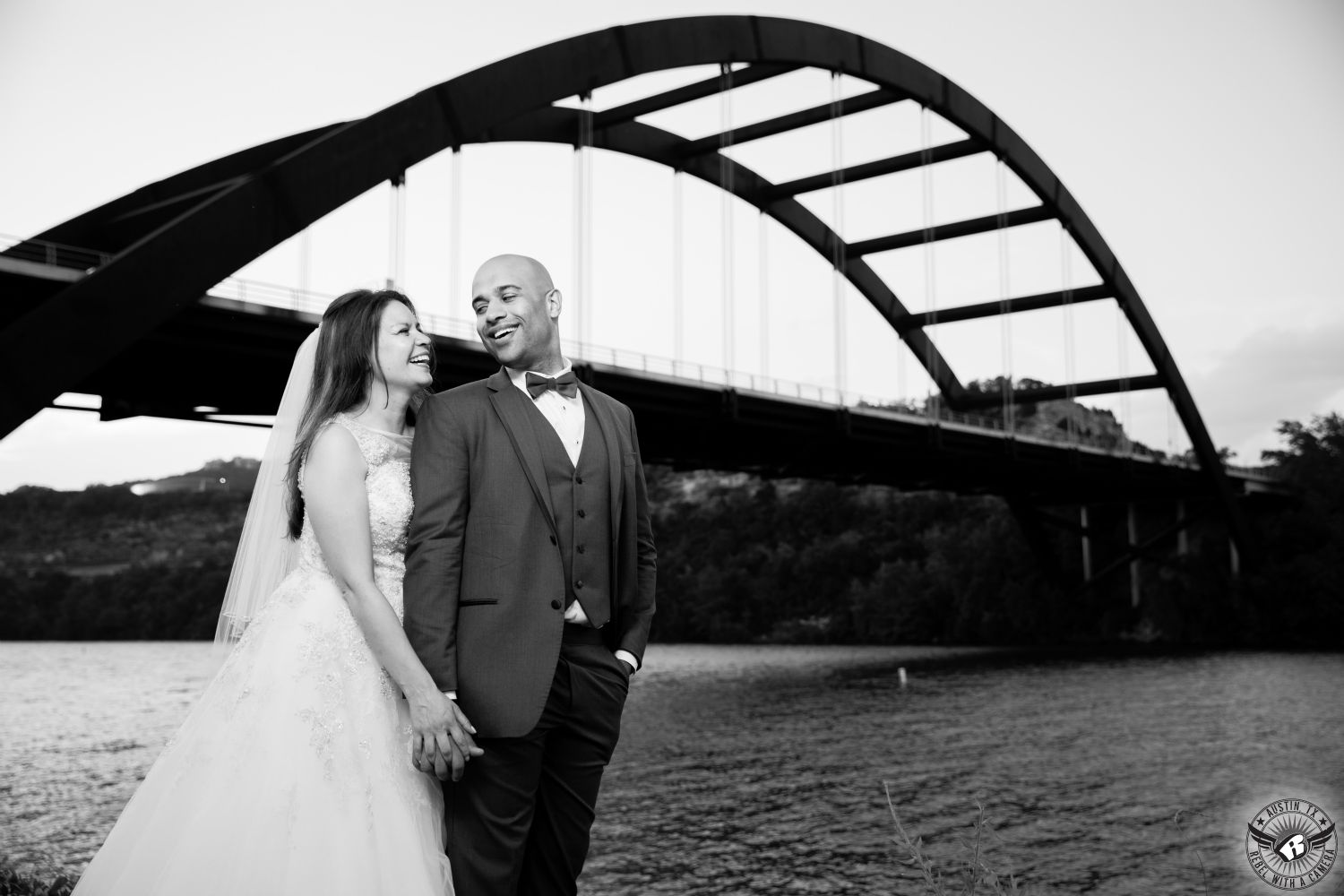 Black and white image of bride looking lovingly at groom wearing grey suit and bowtie in front of Pennybaker Bridge in Austin.