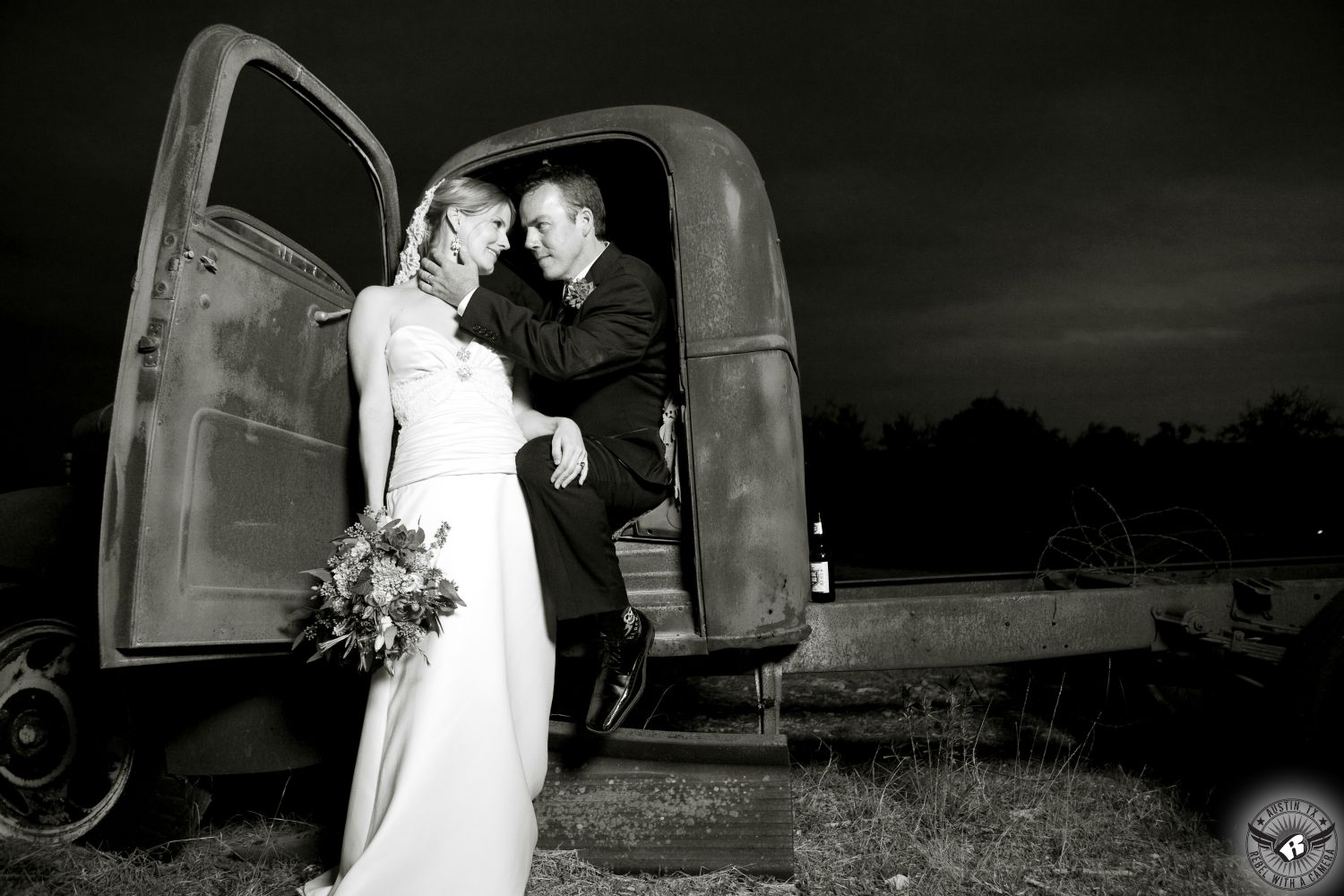 Austin wedding photographer takes picture of groom looking lovingly at bride in sophisticated strapless wedding dress while he sits in the cap of a rusted old pick up truck at Star Hill Ranch the wedding venue in the Texas Hill Country.