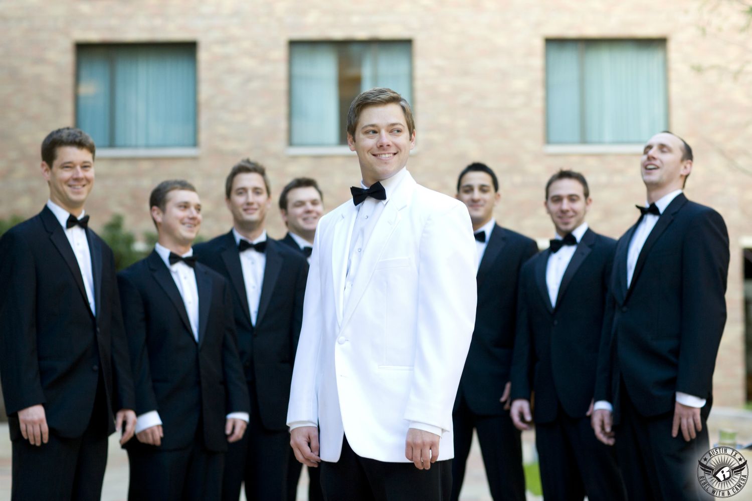 Austin wedding photography of stylish groom in white tuxedo jacket and black bowtie standing in front of groomsmen in black tuxedos at the AT&T Executive Education and Conference Center on the University of Texas at Austin campus.