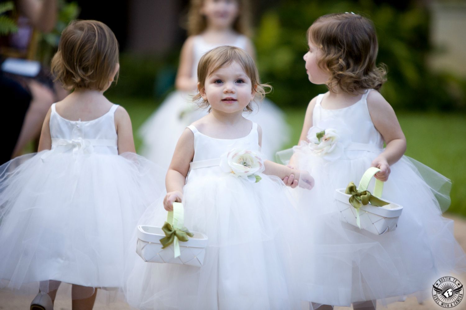 Four adorable flower girls in white tulle walk down the aisle at the Four Seasons in Austin wedding venue outdoor ceremony site during a Jewish wedding.