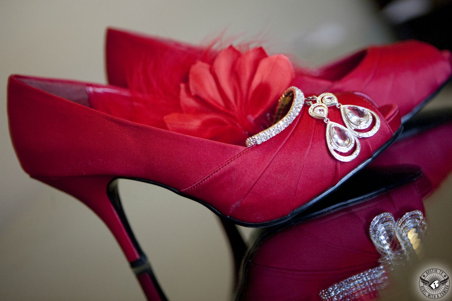 Dramatic, color picture of red high heels, diamond bracelet, dangly diamond earrings, and red feather hairpiece on mirror taken in bride's room by wedding photographer in Austin.