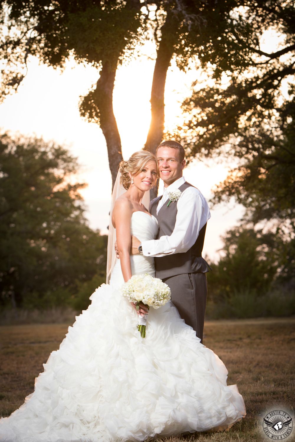Austin wedding photography of beautiful bride with makeup my Maris Malone Calderon and hair by Jen Hoover from Pearl Studio Austin in ruffled wedding gown from Cloud 9 bridal in Georgetown, Texas, with white hydrangea and rose bridal bouquet from Zuzu's Petals and groom in grey tuxedo pants and vest at Kindred Oaks wedding venue in Austin.