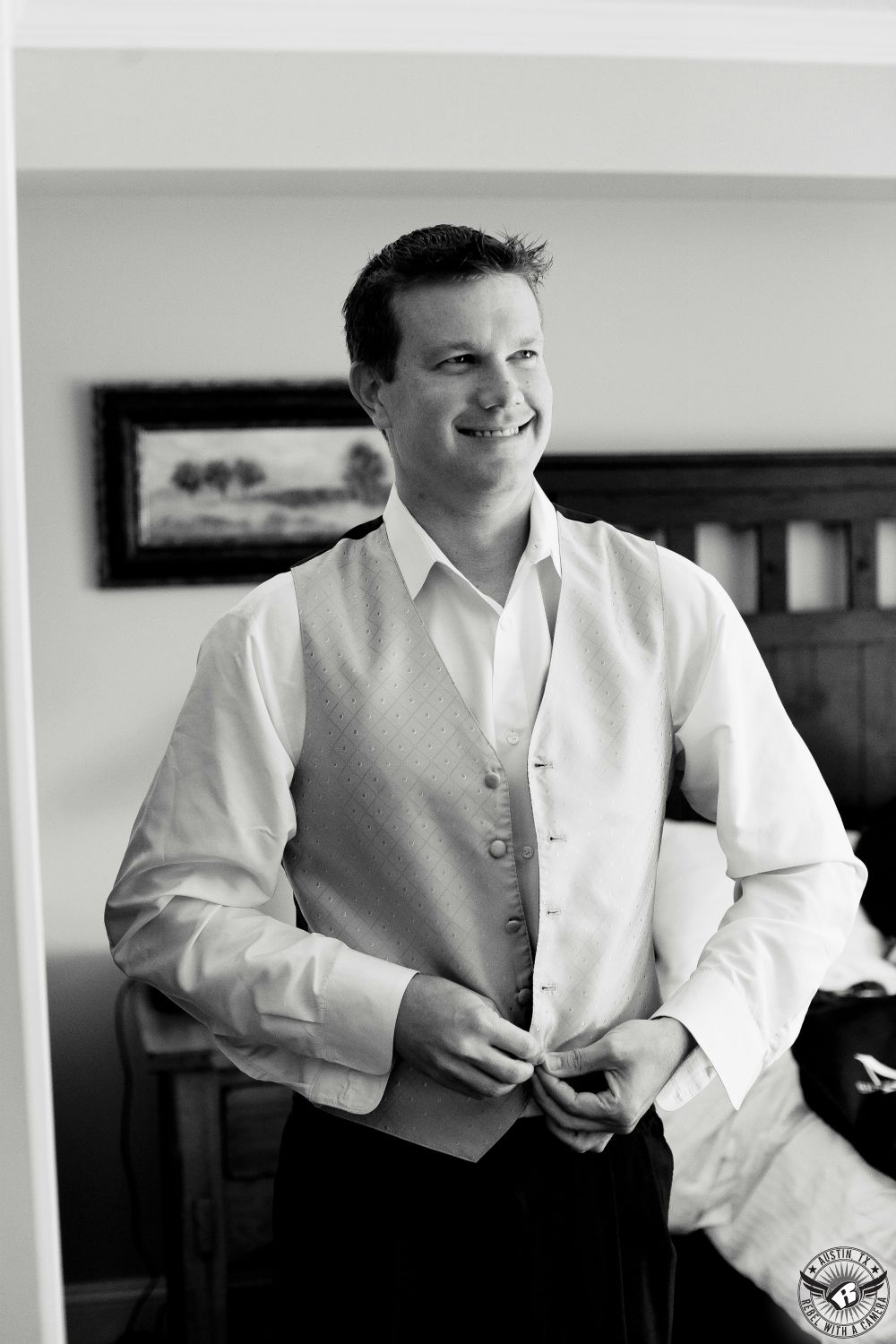 Dramatic wedding picture of groom buttoning up white vest in a hotel room while he gets ready on his wedding day taken by wedding photographer in Austin, Texas.