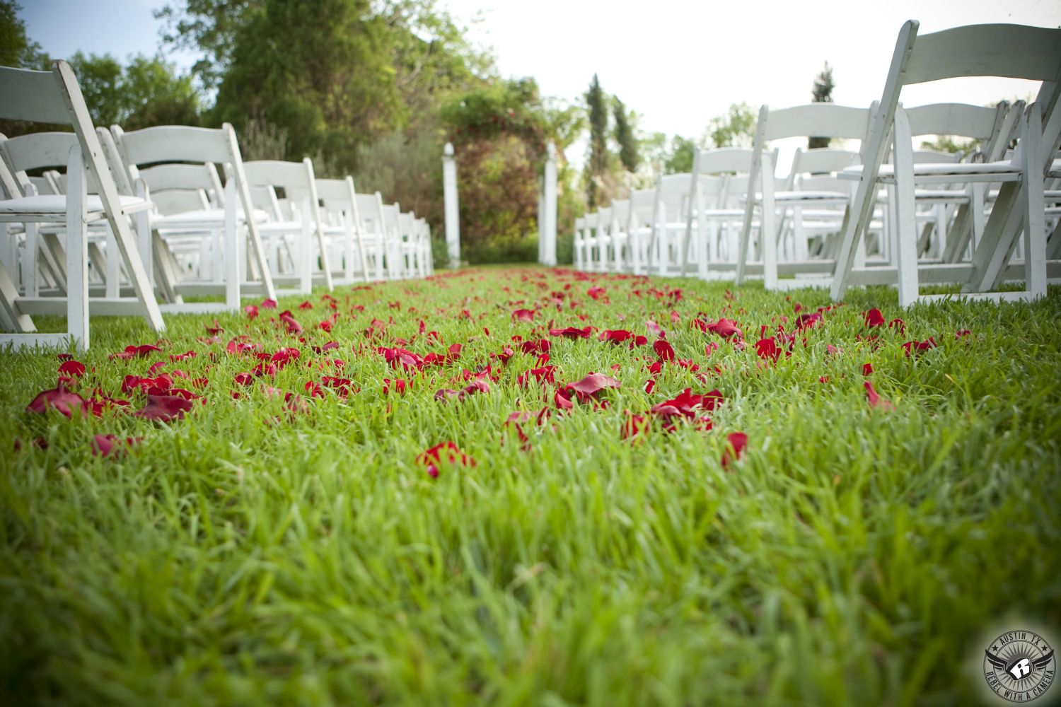 Austin wedding photography of gorgeous outdoor wedding ceremony site with white chairs and green grass strewn with red rose petals with white arbor at the Austin wedding venue Barr Mansion.