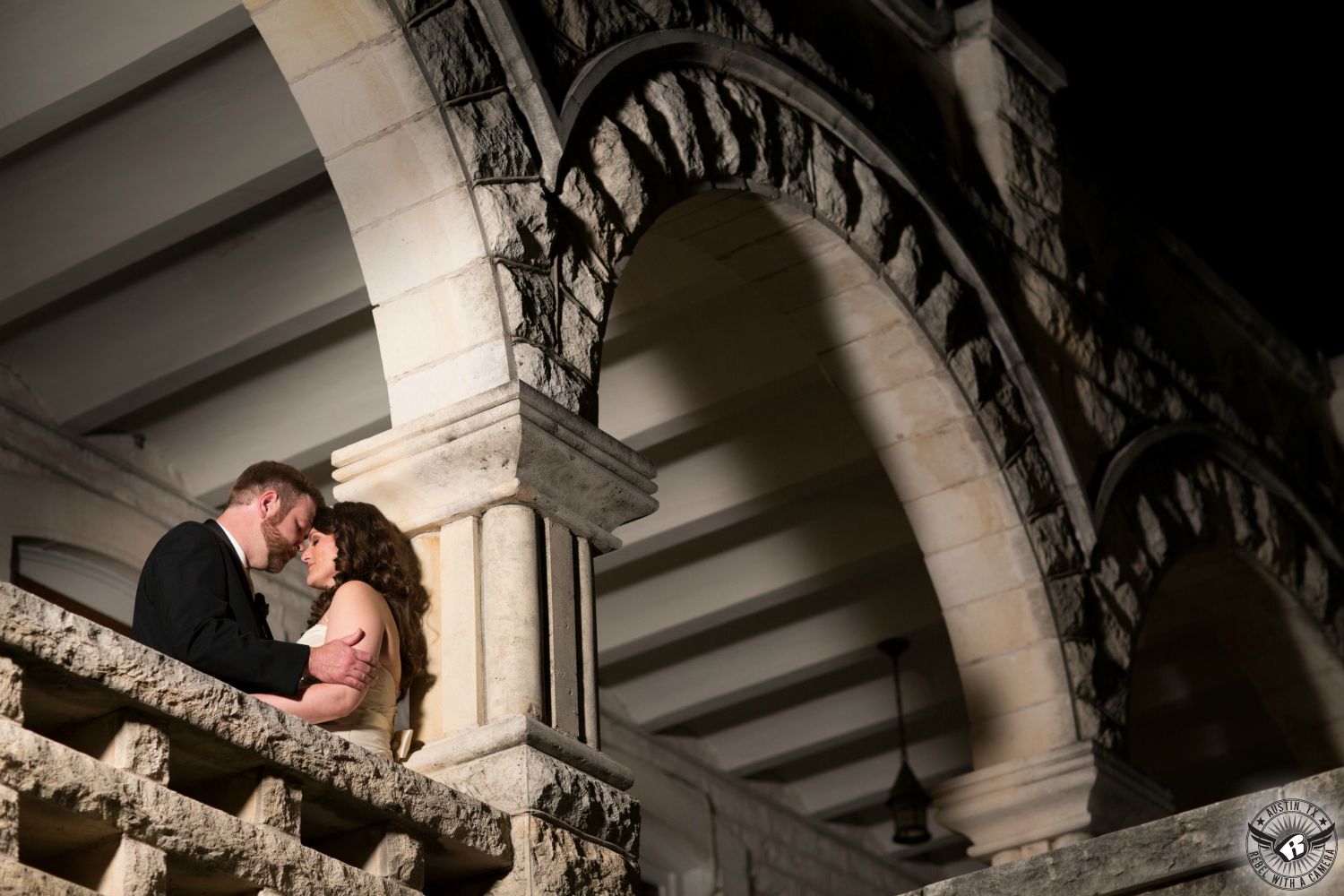 Dramatically lit image of brunette bride and groom with beard in black tuxedo in romantic pose under the arches at Chateau Bellevue wedding venue in downtown Austin, Texas.