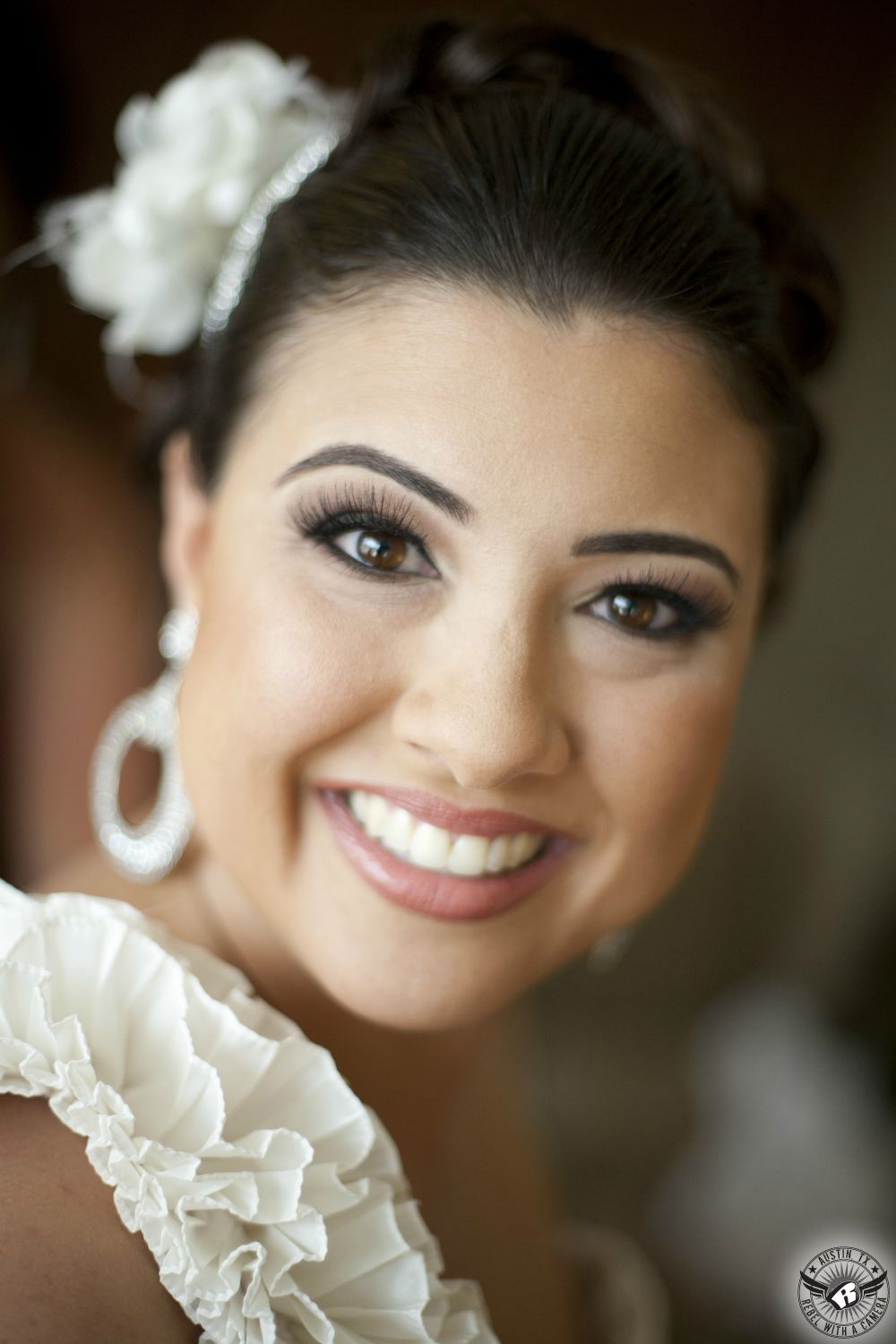 Wedding picture of happy and beatiful Lebenese bride in one shouldered ruffled wedding dress with dangly hoop earrings with flower in her hair in the bride's room at the Westin Galleria in Houston on her wedding day.