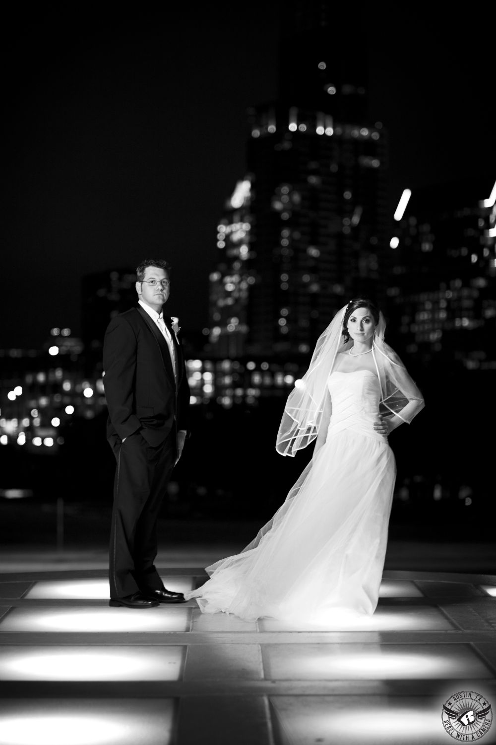 Dramatic portrait of bride and groom on their wedding day at the Long Center standing in front of the Austin city skyline at night taken by Austin wedding photographer, Rebel with a Camera.