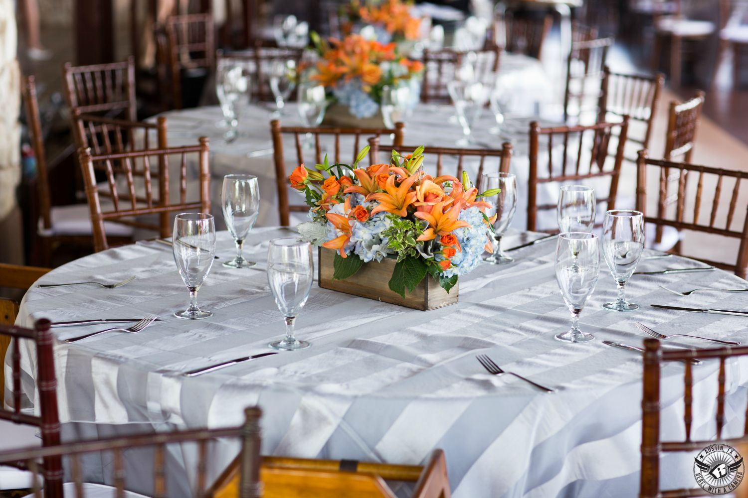 Gorgeous wedding tablescape with grey striped linens, dark wooden chivari chairs, and orange lily floral and light blue hydrangea centerpieces by Bouquets of Austin on the deck at Nature's Point, the Austin wedding venue on Lake Travis.