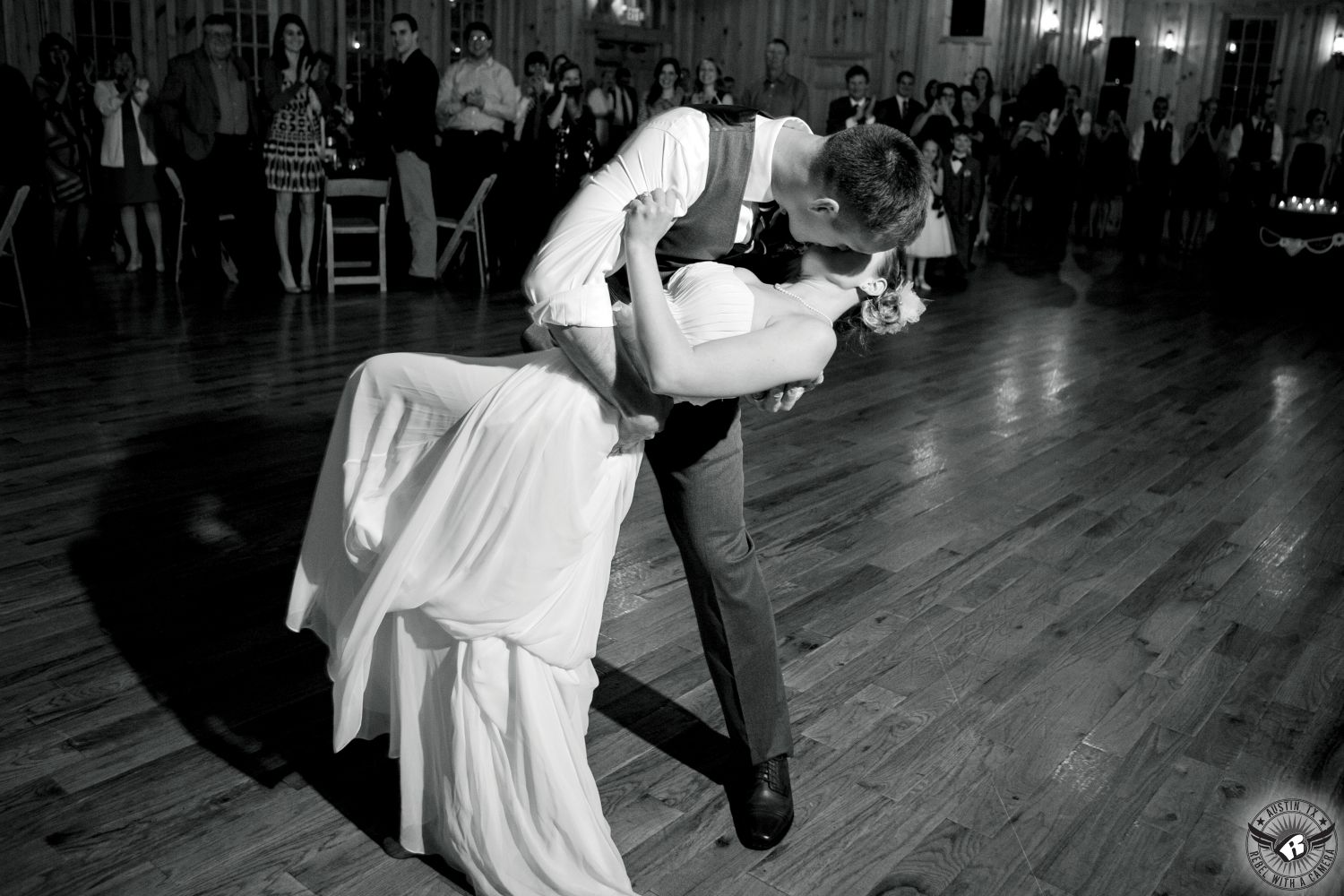 Black and white pciture of groom dipping bride and kisses her as he dips her during their first dance at Texas Old Town in Sage Hall at their wedding reception taken by Austin wedding photographer, Rebel with a Camera.