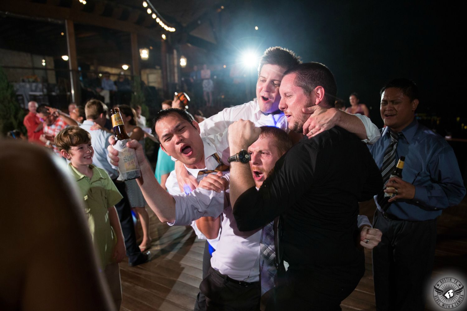 Austin wedding photography of super happy guys drinking Shiner beer dancing to the tunes of Live Oak DJ at wedding reception on the lower deck at Austin wedding venue Nature's Point on the shores of Lake Travis.