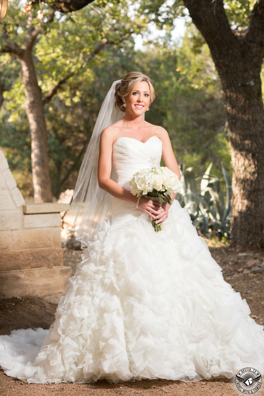 Stunning blonde bride in ruffled dress from Cloud 9 Bridal in Georgetown, Texas, and makeup by Maris Malone Calderon and hair styled by Jen Hoover of Pearl Studio in Austin with white bridal bouquet by Zuzu's Petals at Kindred Oaks Life Changing wedding venue in Central Texas.