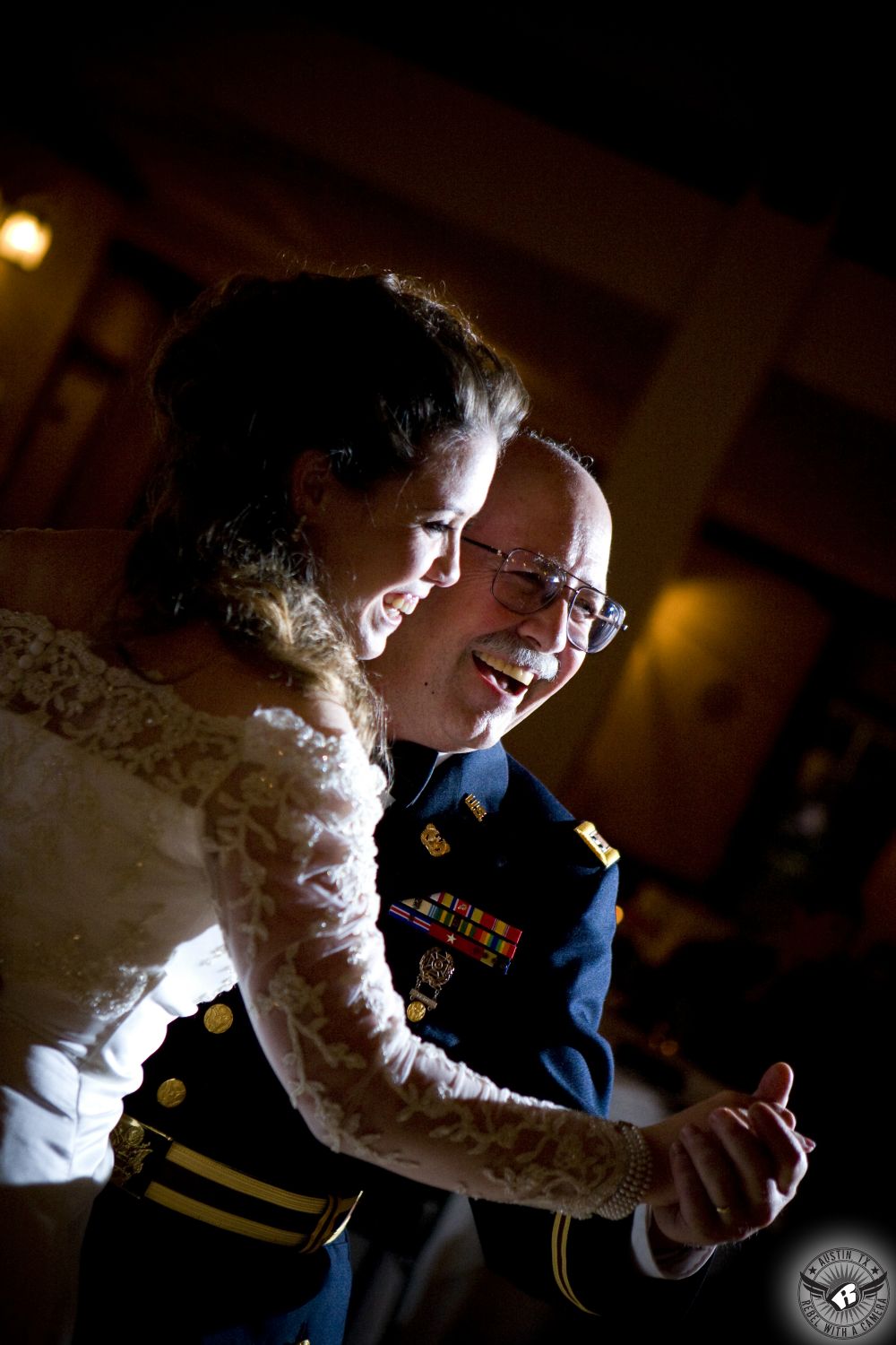 Bride in lace sleeved wedding dress and her father in military dress blues dance together at wedding reception at Star Ranch Golf Club in Hutto Texas with dramatic lighting.