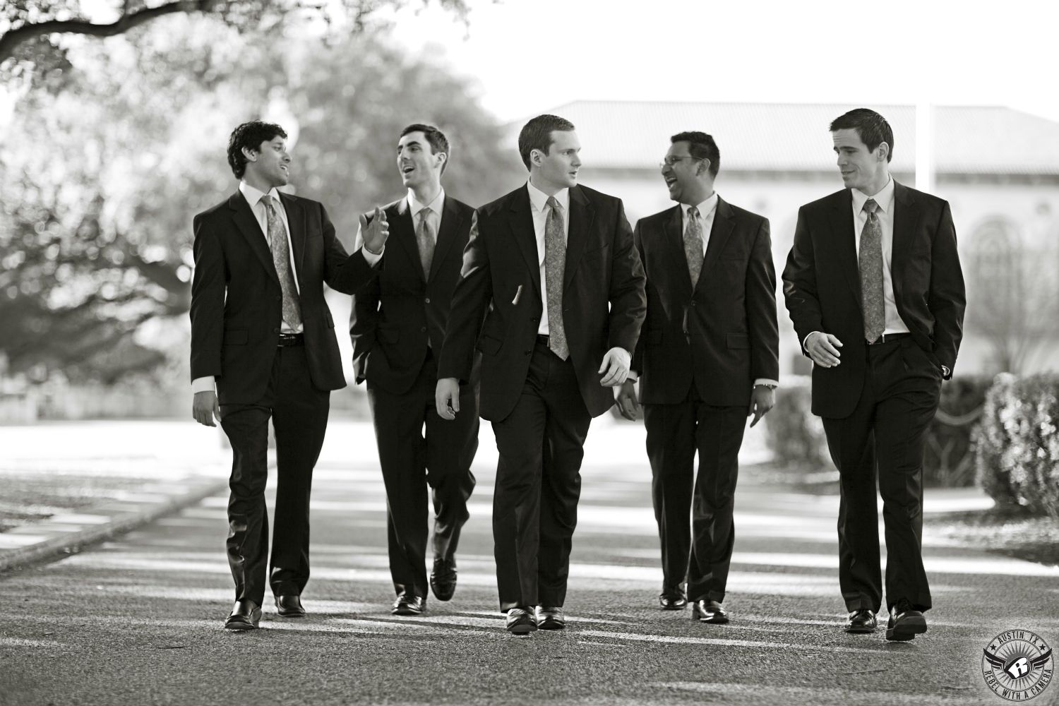 Black and white picture of groom walking with groomsmen on the University of Texas campus on his wedding day in Austin taken by Austin wedding photographer.