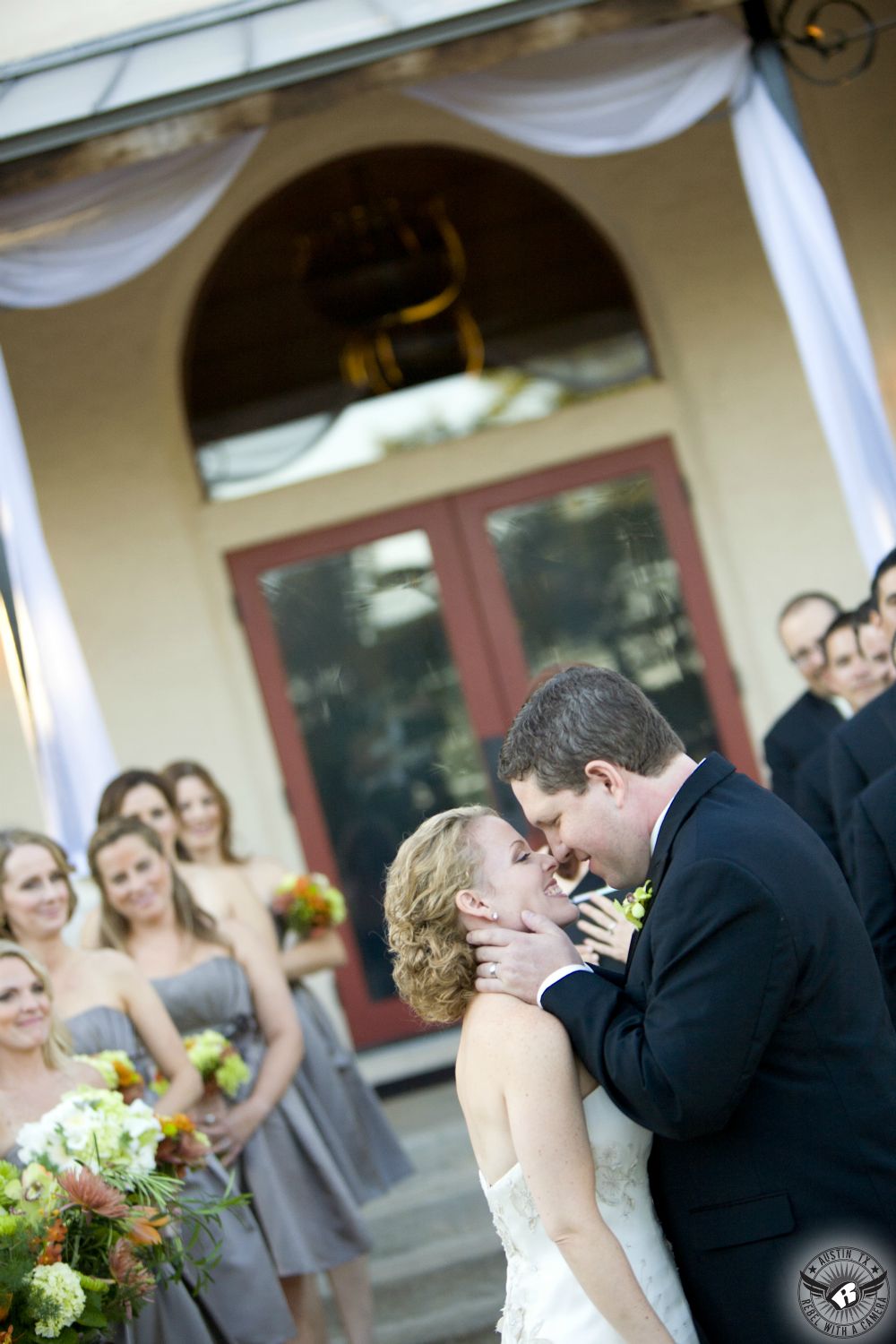 Bride and groom kiss during their outdoor wedding ceremony with bridesmaids bouquets by Design by Sage Austin wedding florist at Hamilton Twelve wedding venue in the Hill Country.