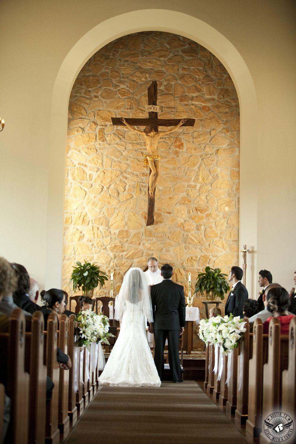 Austin wedding photography of bride and groom standing on the altar and saying their wedding views during Catholic wedding ceremony with priest at the Queen of Angels Chapel in Spicewood, Texas.