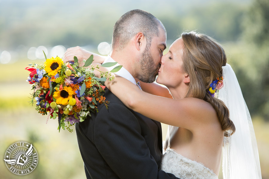 Wedding pictures at Thurman's Mansion at the Salt Lick - bride and groom kiss with colorful wildflower bouquet by Verbena Floral Design