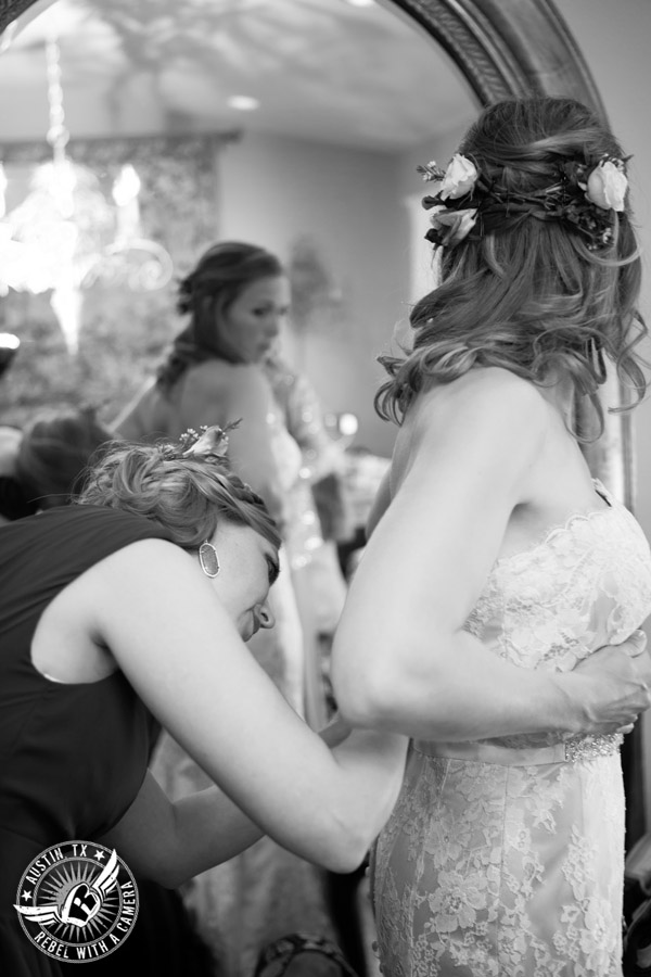 Wedding pictures at Thurman's Mansion at the Salt Lick - maid of honor helps bride put on wedding dress in the bride's room