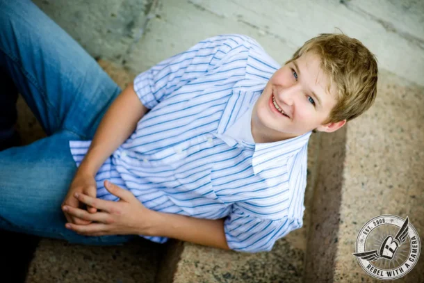 Smiling senior in a striped shirt seated on stone steps in Austin, TX.