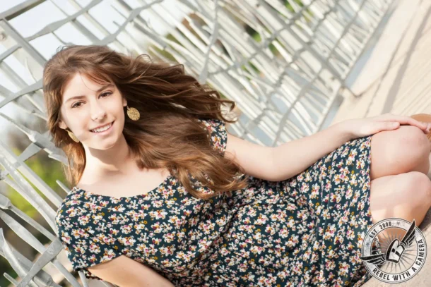 young woman in a floral dress reclining beside a metal fence in Austin, TX.