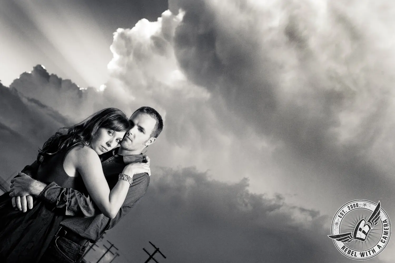 Black and white couple embracing beneath dramatic clouds in Austin, TX.