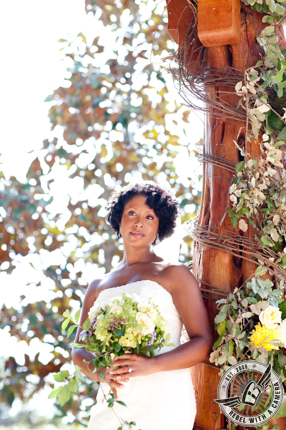 Bride in a white dress holding a bouquet beside a vine-covered wooden structure in Austin, TX.
