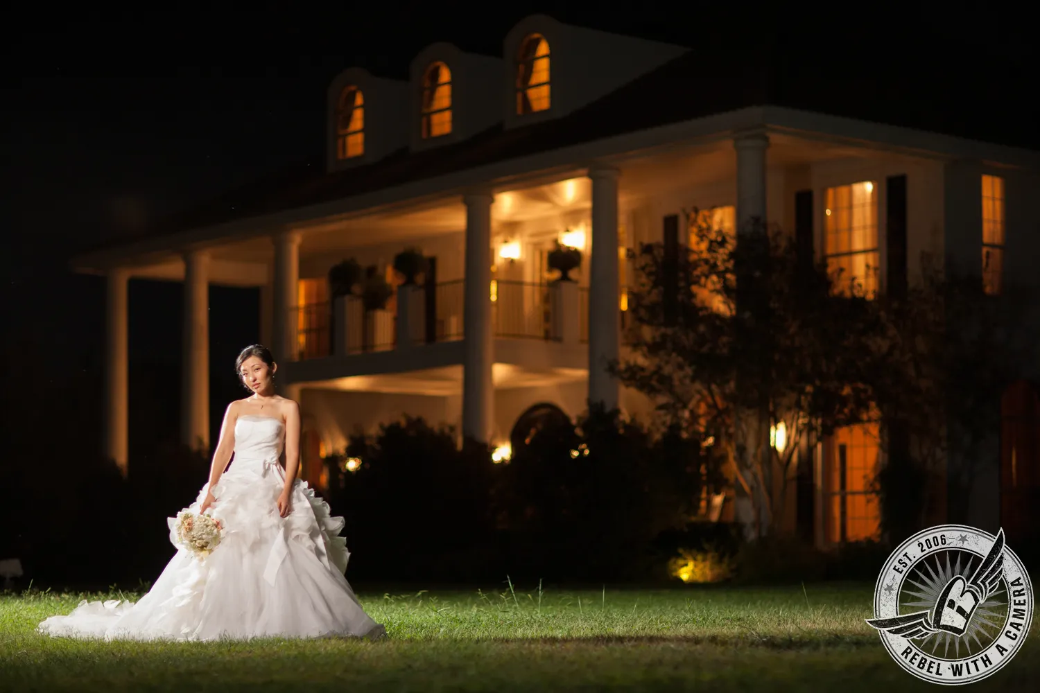 Bride in a white wedding dress holding a bouquet on the lawn of a lit house at night in Austin, TX.