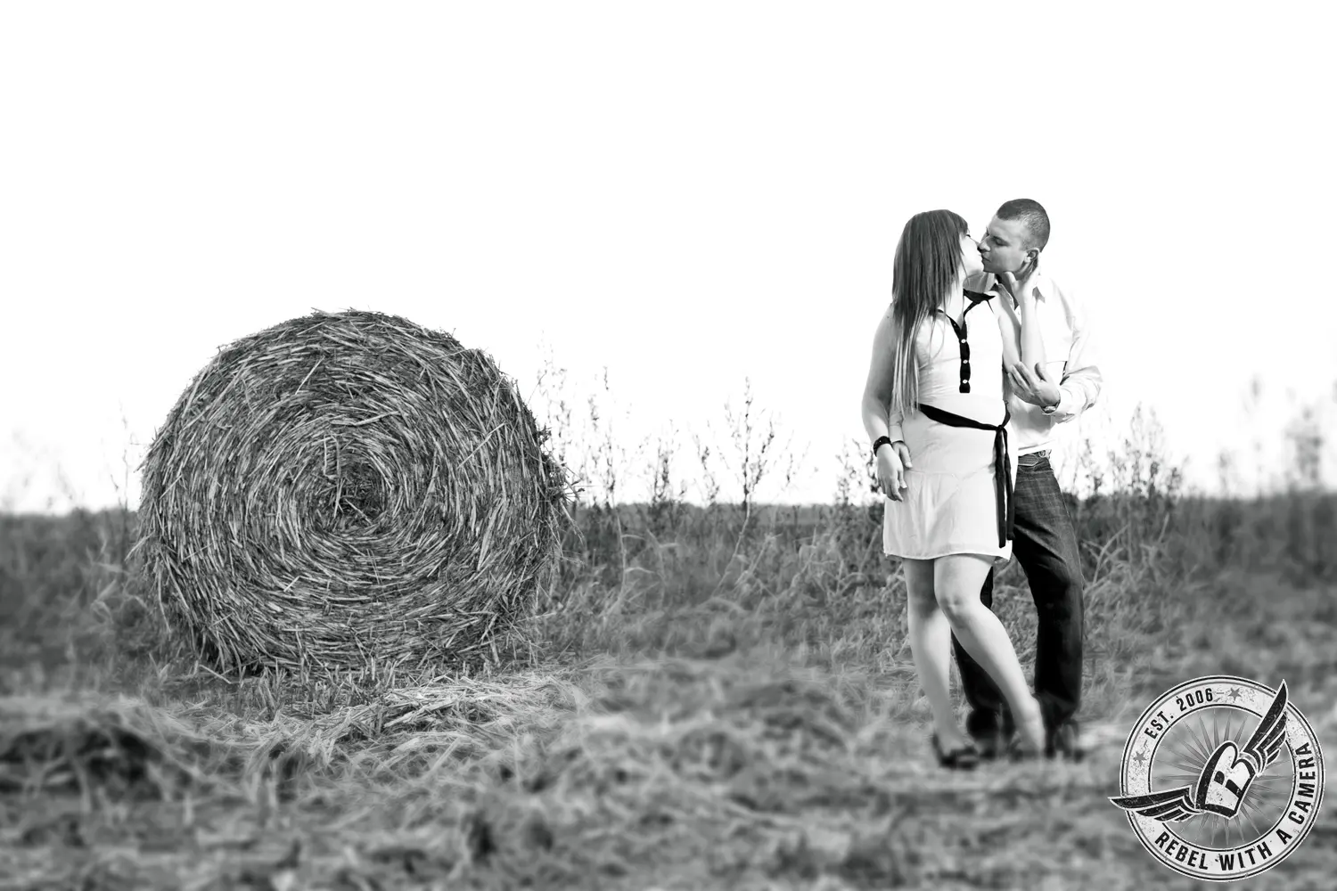 Black and white couple kissing beside a round hay bale in Austin, TX.