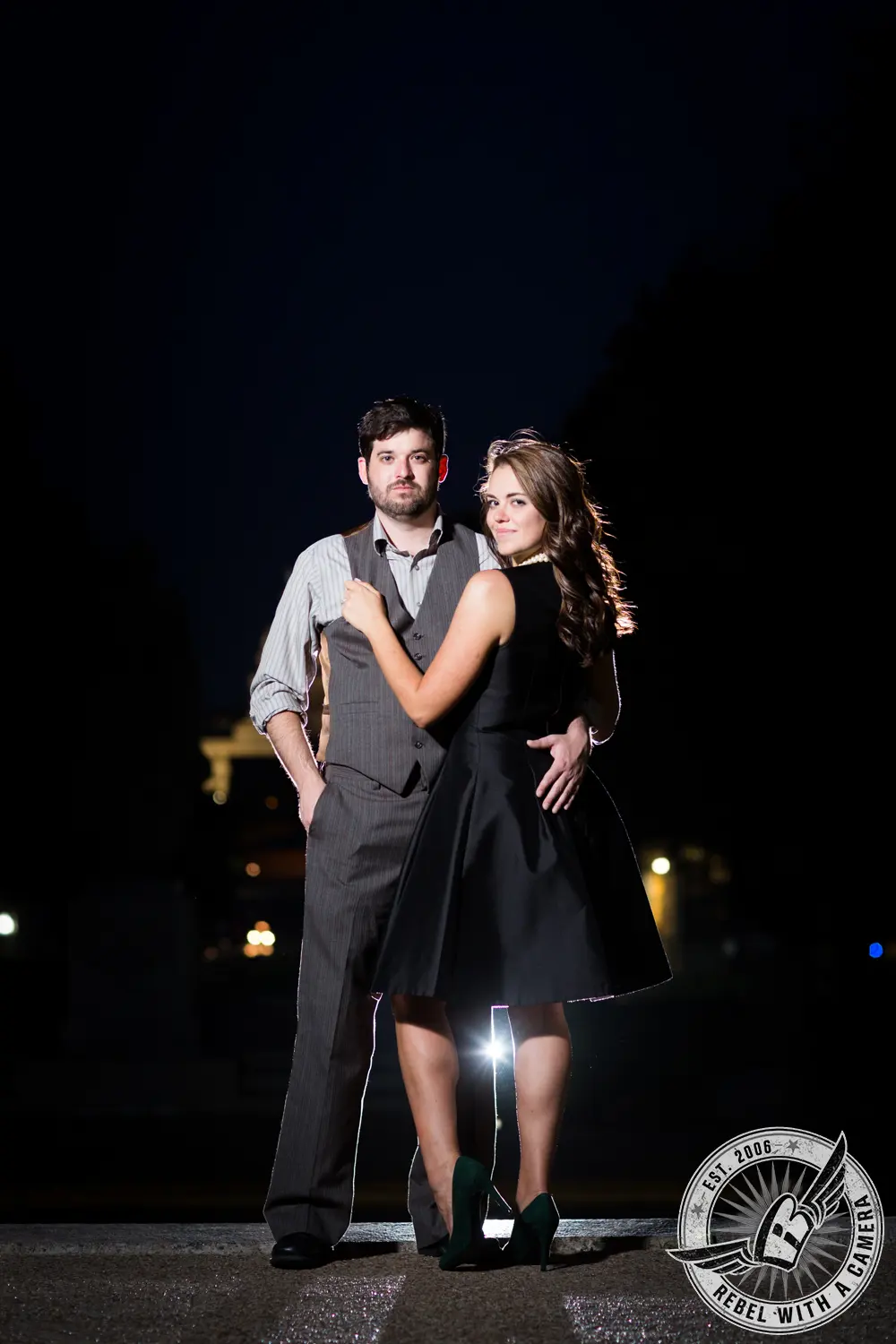 Couple posing together at night with city lights behind them