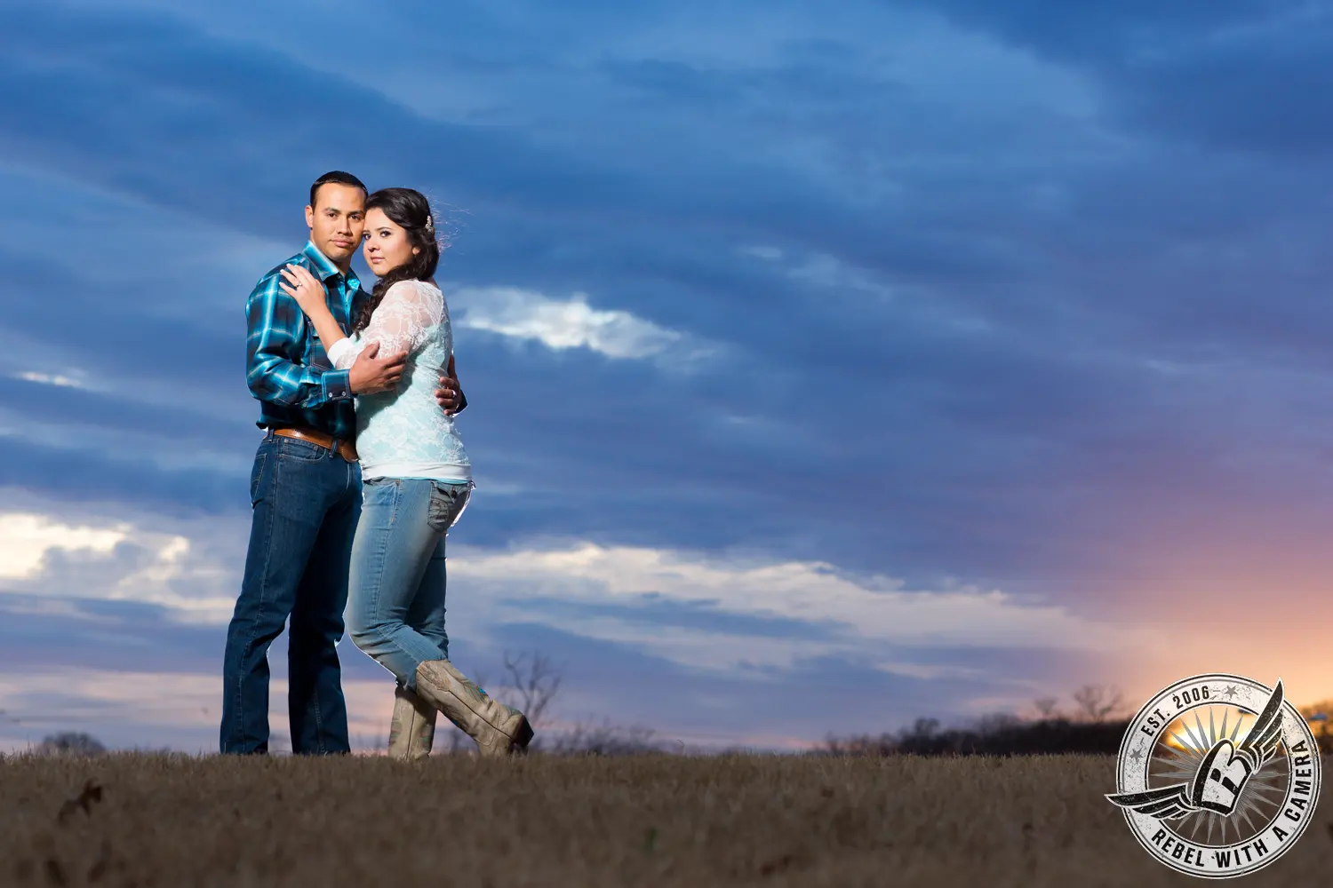 Couple embracing in a grassy field beneath a dramatic evening sky