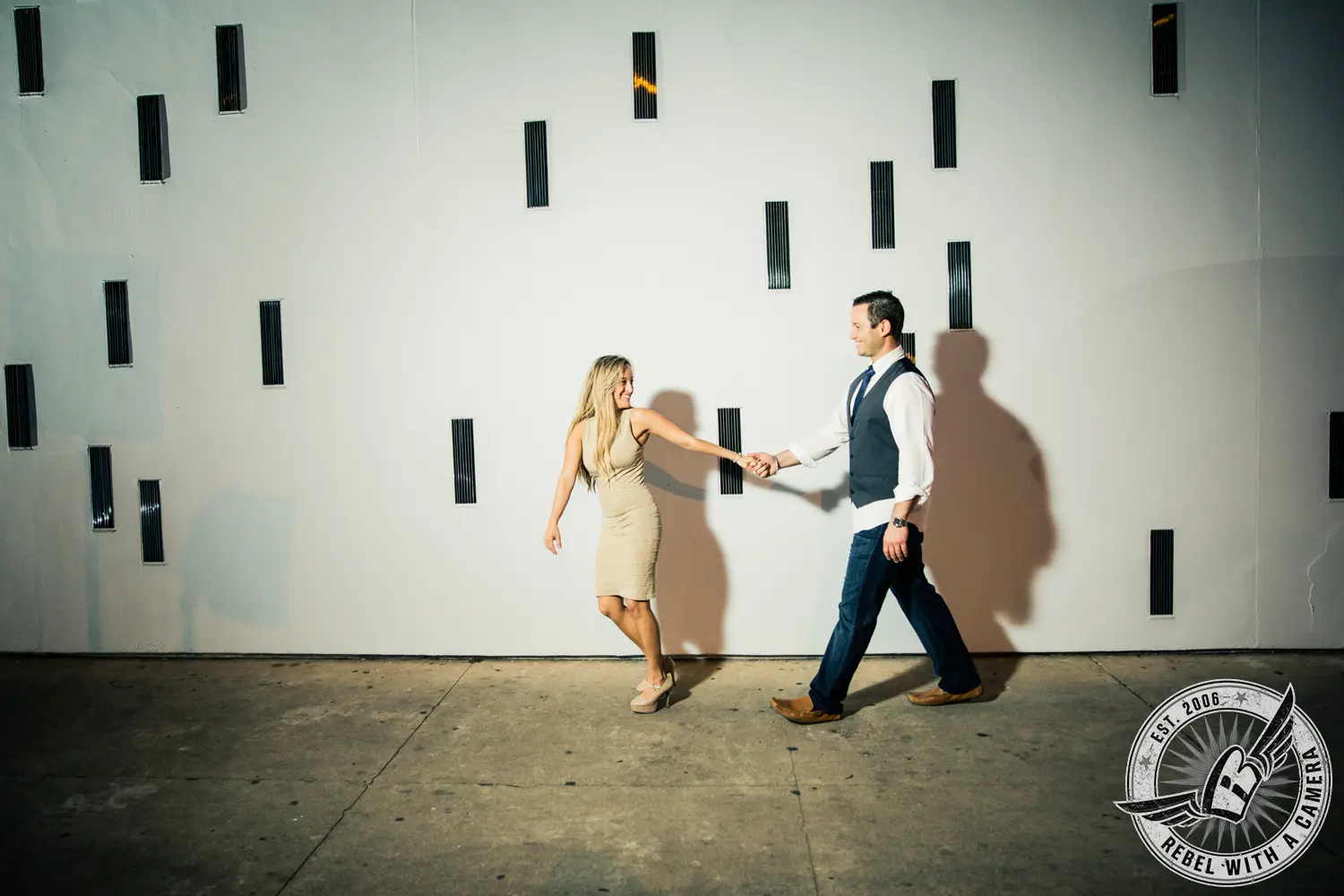 Couple walking hand in hand beside a modern wall in Austin, TX.