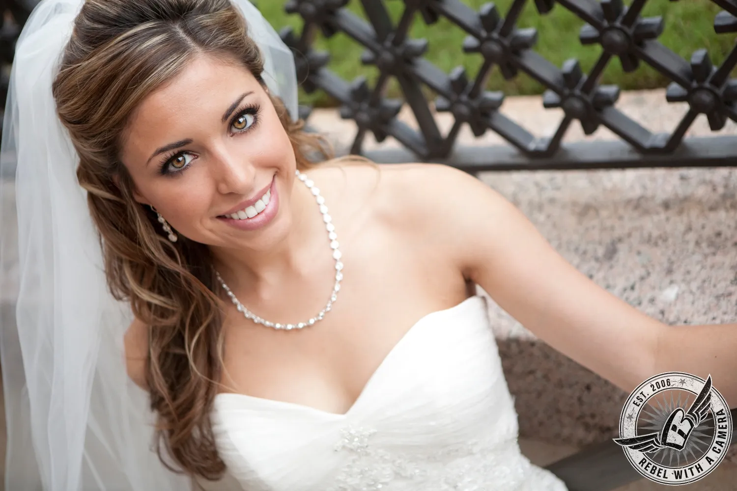 Smiling bride in a white wedding dress reclining beside a wrought iron railing in Austin, Texas.