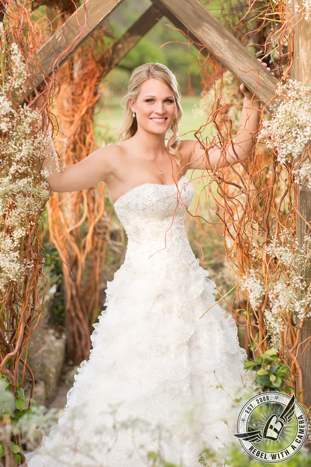 Smiling bride in a white wedding dress framed by a rustic floral arch in Austin, TX.